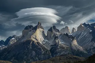 Granite spires in Patagonia under a lenticular cloud in a violent wind.