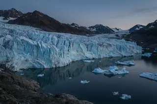 A retreating glacier front calving into dark water under a night sky.