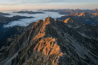 A jagged alpine ridge lit orange by the last sunlight above a sea of cloud.