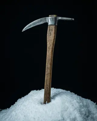 A single ice axe standing upright in snow against a black background.