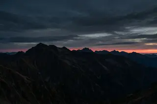 A line of climbers and a thin red sunrise line behind a dark mountain silhouette.