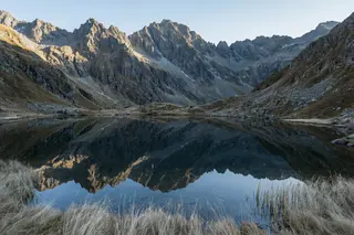 Still alpine lake perfectly mirroring a jagged mountain range in the late afternoon.
