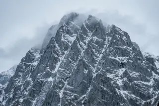 A snow-covered north face emerging from clouds under a pale grey sky.