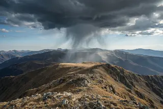 A small dark storm cloud dropping rain over a sunlit mountain plateau.