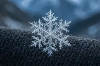 A macro photograph of a snow crystal on a dark glove.